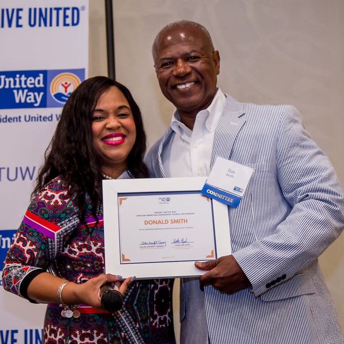 "Sonia Hanson and Don Smith stand and smile as Smith holds up his recently received award certificate."