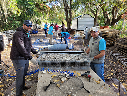 Two volunteers at the SCDNR Oyster Scoring gathering oyster shells together, looking at camera and smiling