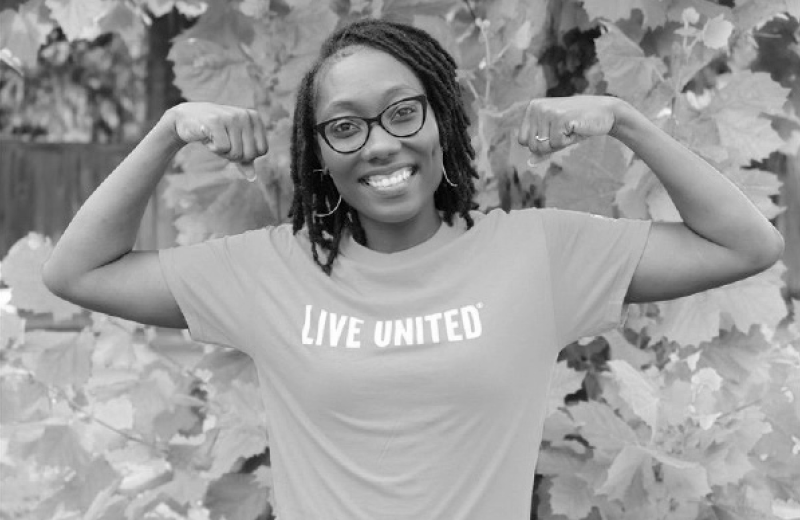 Black and white photo of a Trident United Way staff member wearing a shirt that says LIVE UNITED making muscle arms