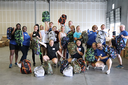 TUW volunteers/staff smiling holding backpacks full of supplies for kids