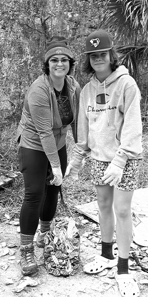 black and white photo of two volunteers outside picking up oyster shells with gloves on