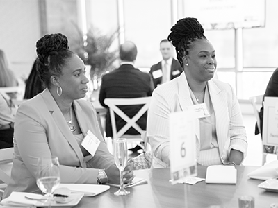 Black and white photo of two women sitting next to each other at a table during an event