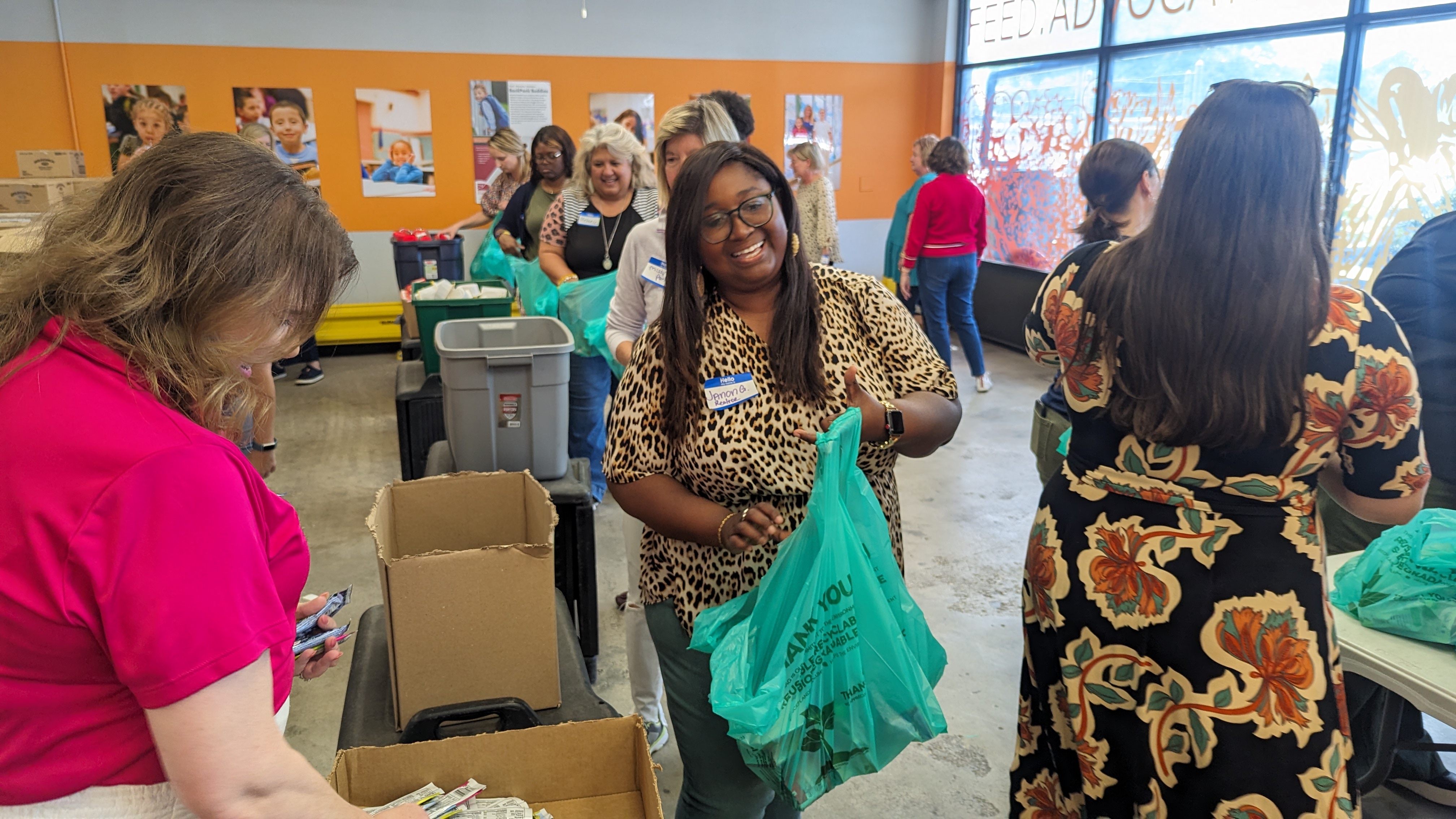 A smiling volunteer packs kits with her teammates in a commercial space.