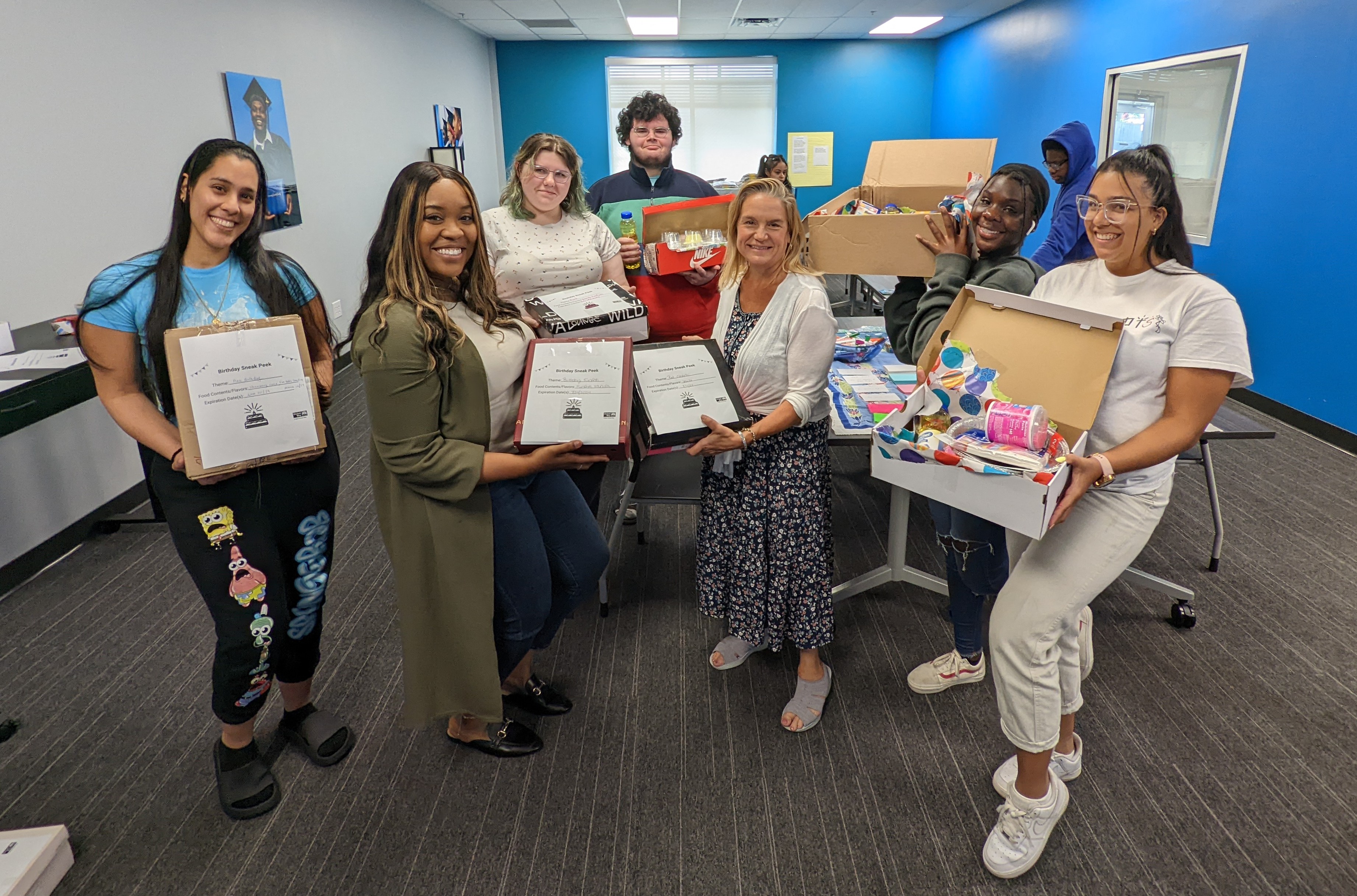 A group of volunteers smile and hold their finished Birthday-In-a-Boxes after volunteering.
