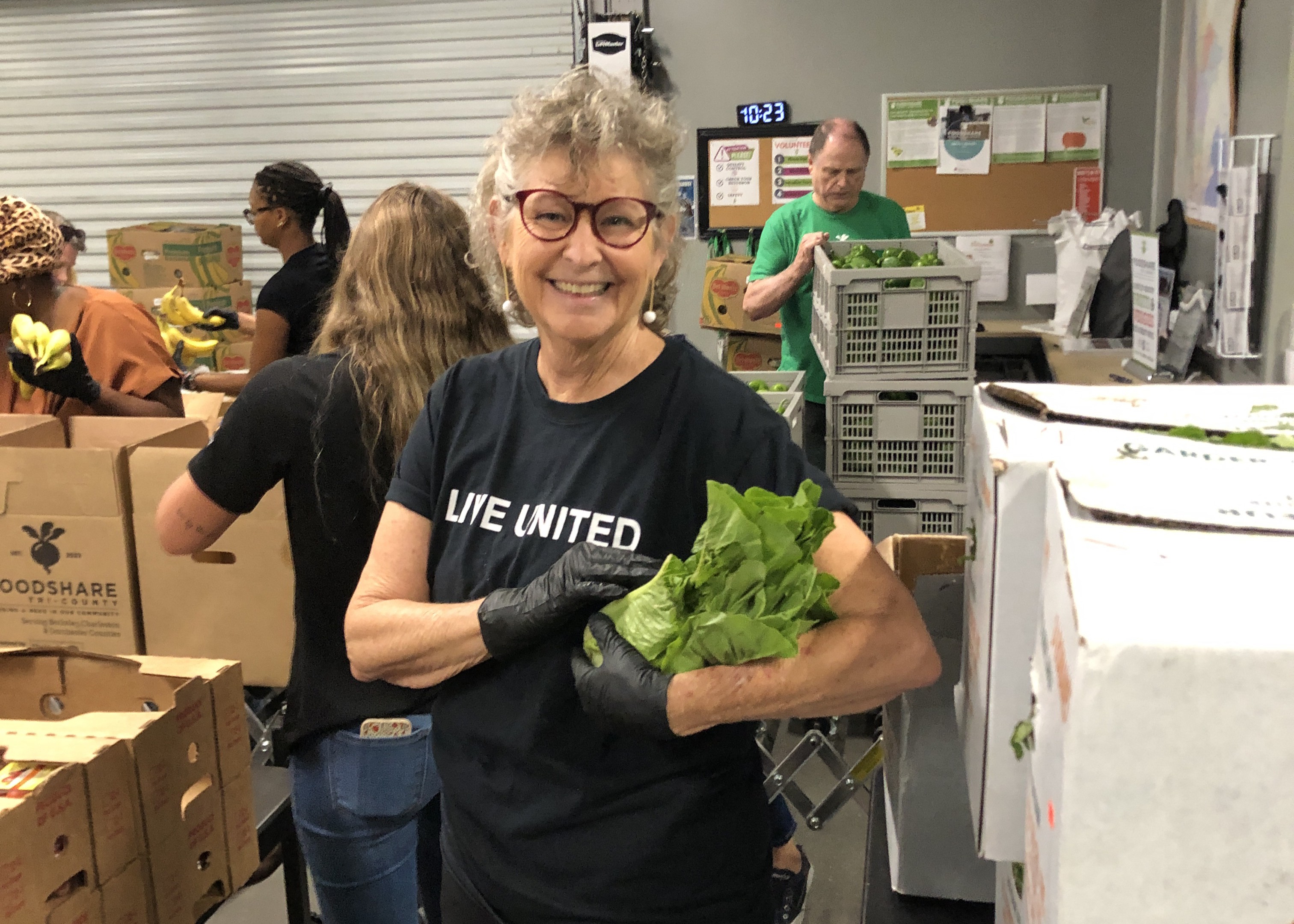 A volunteer holds produce while smiling and packing fresh food boxes.