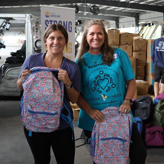 Two women holding backpacks smiling.
