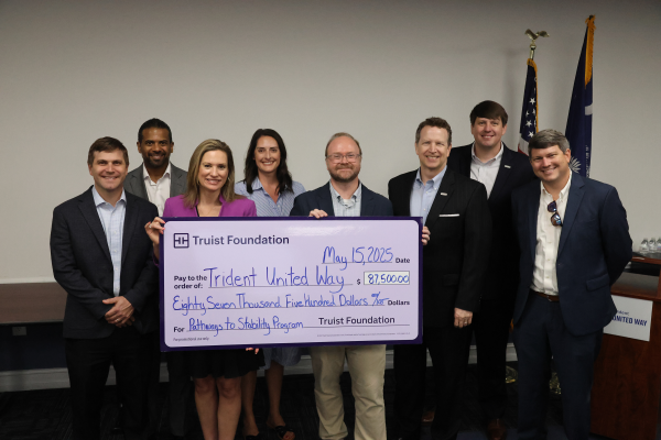 A group of 7 Truist Foundation members stand next to DJ Hampton, President and CEO of TUW. They are all standing behind a large check written to TUW from Truist for $87,500. The check is for the Pathways to Stability Program.