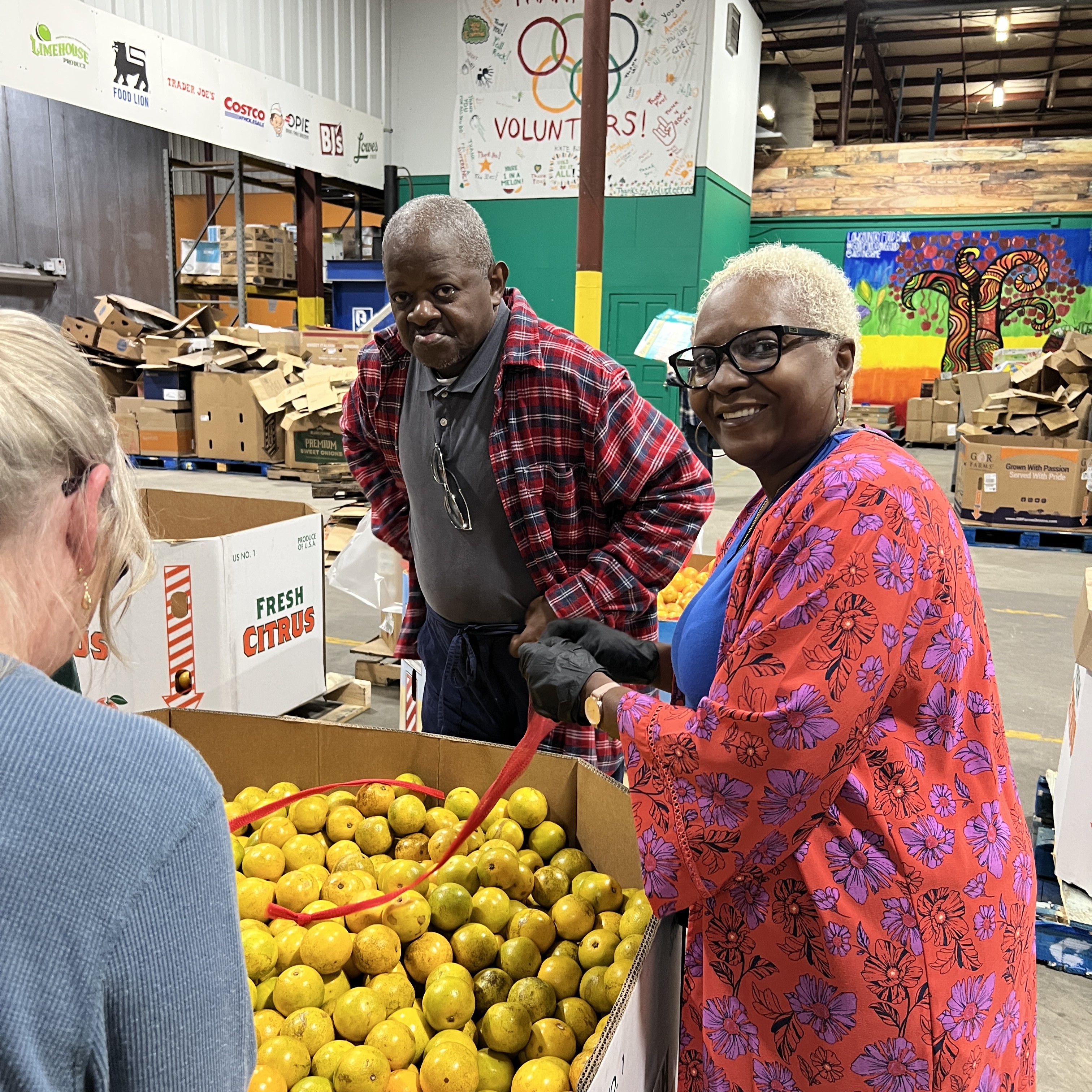 Two smiling volunteers help pack fresh produce while smiling at the camera.