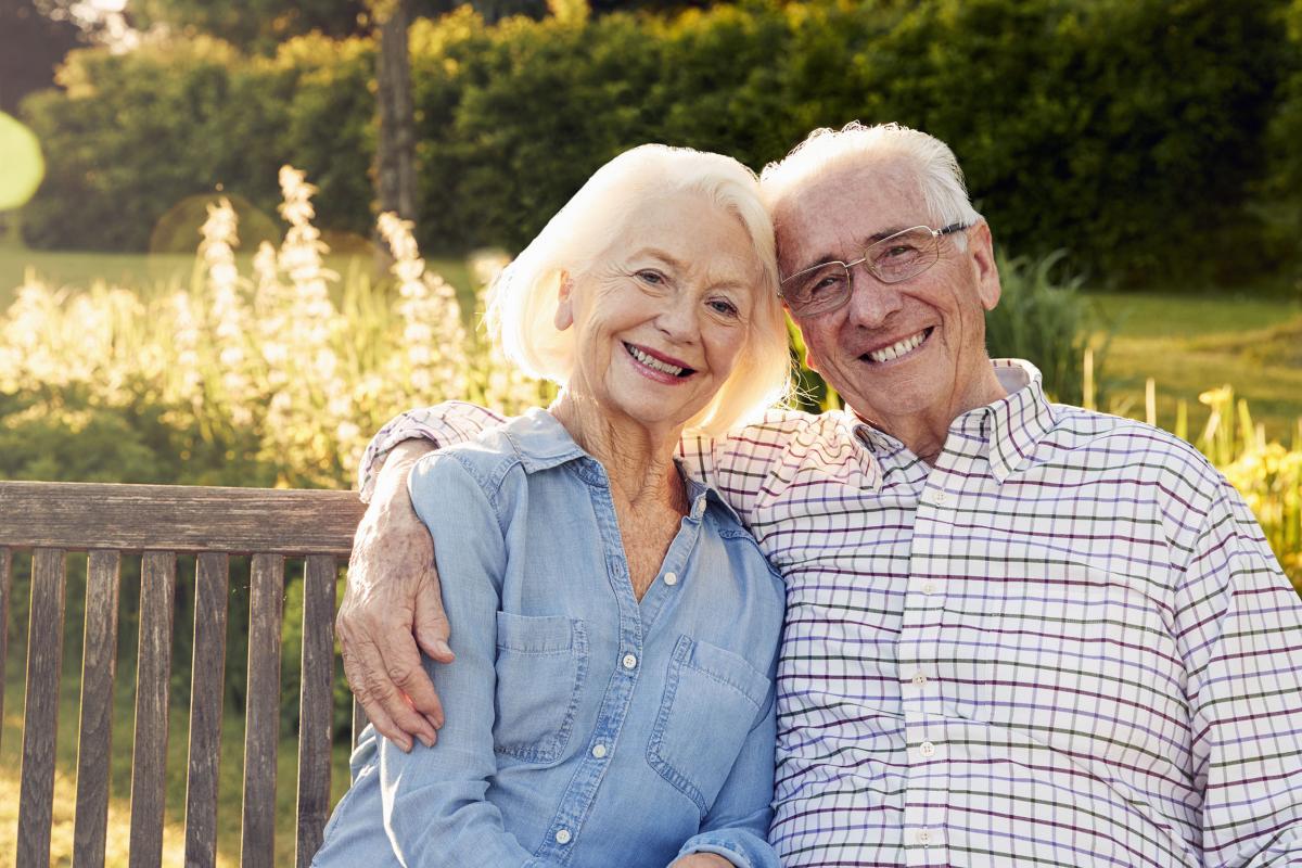 elderly couple sitting on a bench outside, embracing and smiling