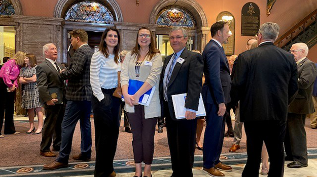 Photo of Trident United Way staff Katie Reams, Naomi Zeiset and Brad Davis standing in the center of the SC State House. They are wearing business professional attire and holding binders and notebooks, smiling at camera