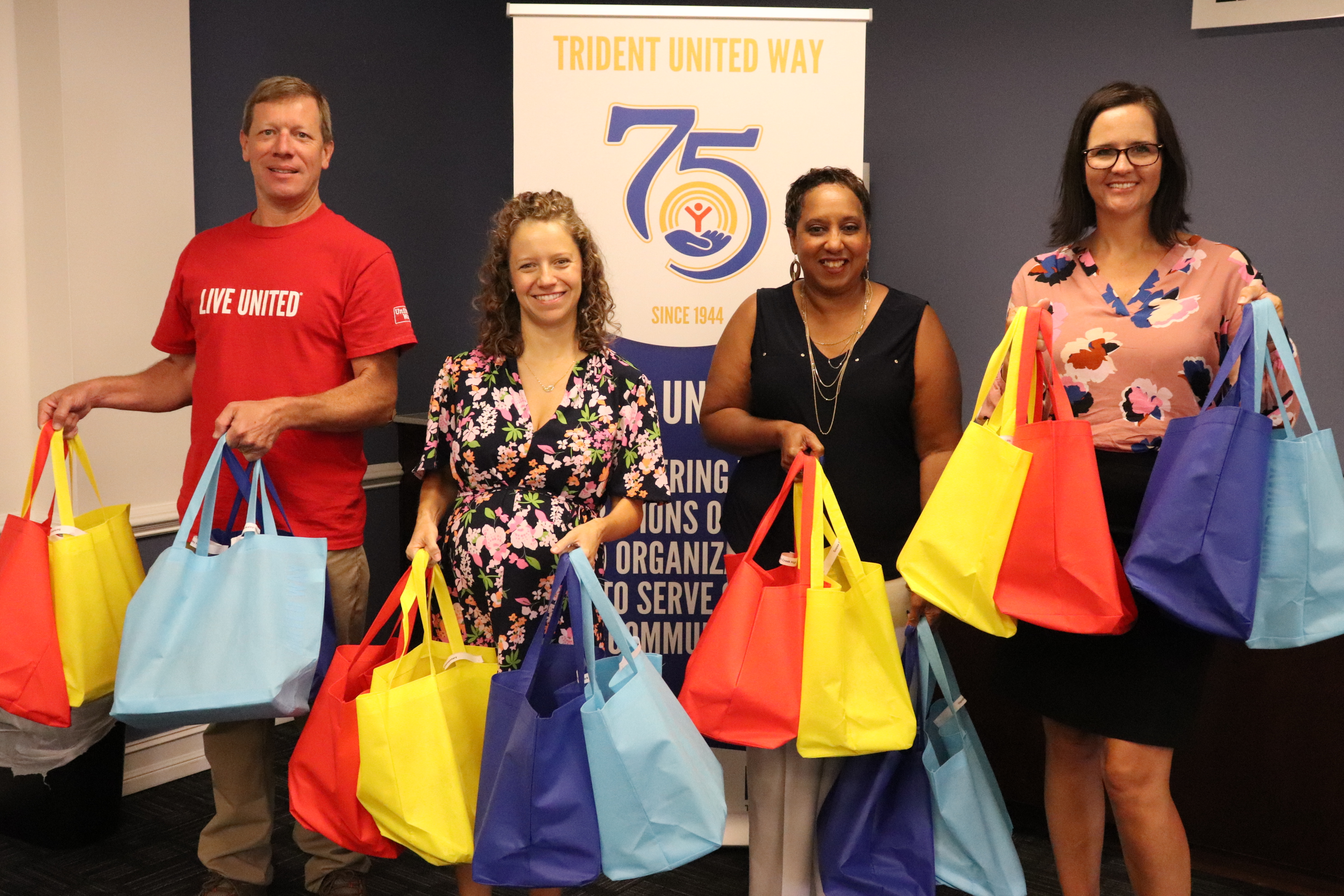 group of TUW staff holding bags with TUW swag to be distributed for campaign standing in front of a TUW banner