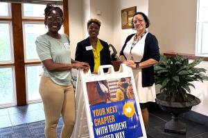 3 women standing around a sign that reads Your Next Chapter with Trident United Way
