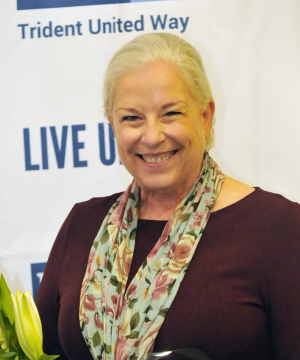 Cathy standing in a brown shirt and scarf. She is smiling and looking at the camera.