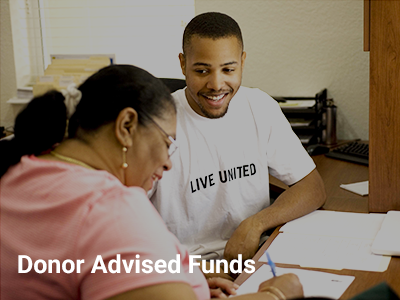 Photo of a man wearing a Live United shirt assisting a woman completing paperwork. Donor Advised Funds in written on the bottom of the photo