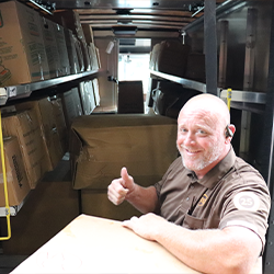 UPS member moving a box filled with packed backpacks into truck giving thumbs up