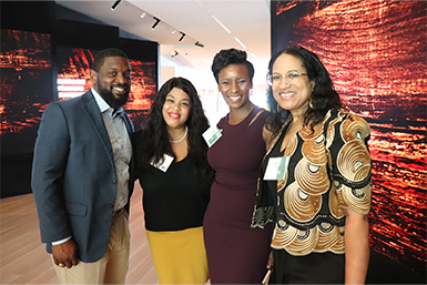 Group of one man and three women standing together and smiling inside of the International African American Museum