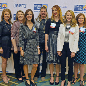 Photo of the Women United Steering Committee at the awards lunch standing in front of a Trident United Way step and repeat smiling