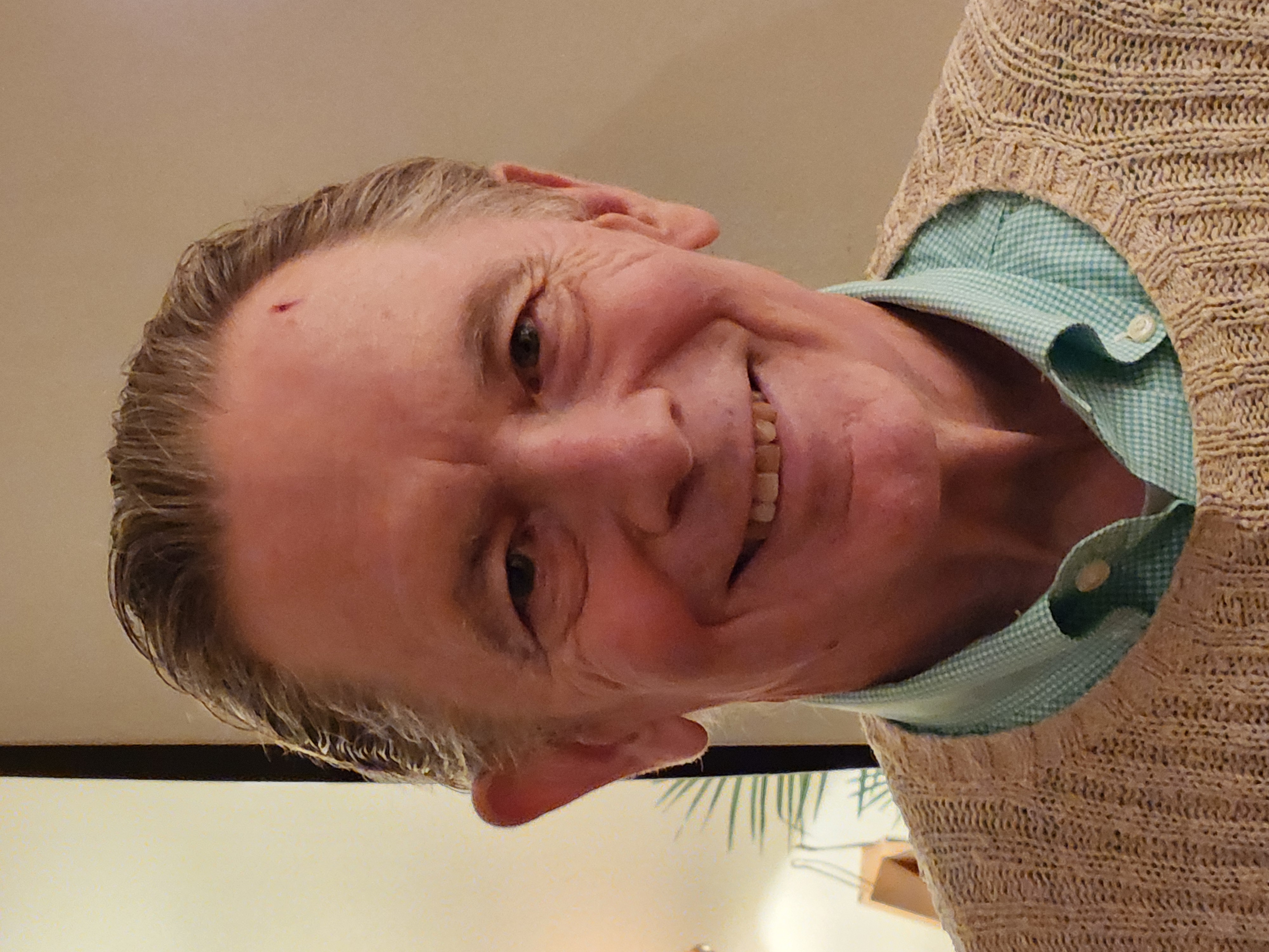 Stephan Christiansen has short hair, wears a green printed button up under a beige sweater