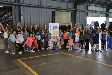 Photo of a group of volunteers holding backpacks. Many volunteers have their arms in the air to celebrate the accomplishment.