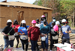 AmeriCorps members holding tools and hard hats in front of a Habitat for Humanity house