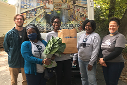 AmeriCorps Members wearing AmeriCorps shirts holding grocery bags of food in front of a Lowcountry Food Bank truck