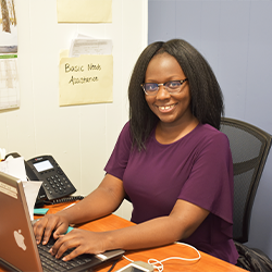 Photo of a woman sitting at a desk with her hands on a laptop keyboard, smiling and ready to assist a client