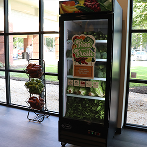 A free and fresh fridge at a local library, filled with fresh fruits and vegetables next to a three tiered stand containing additional produce baskets