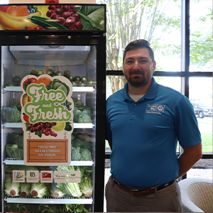 Trident United Way staff member wearing a blue TUW polo standing next to a free and fresh fridge