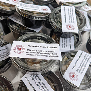 A pile of small plastic containers with lids containg Pasta with Beans& Greens