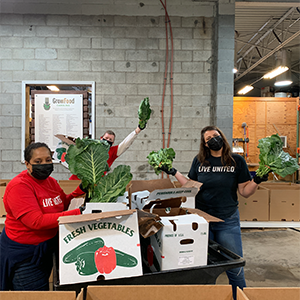 A group of three individuals wearing Live United shirts packing large cardboard boxes with produce at a warehouse