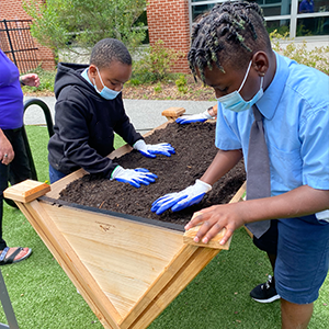 Two male students are smoothing dirt in a garden bed