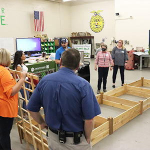 Several teachers stand around a wooden outline for a garden bed listening to three instrutors, one is holding a trellis