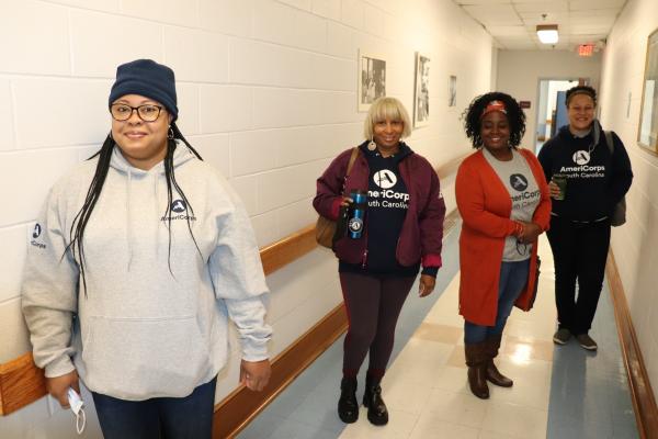 AmeriCorps members pose for a photo in the hallway of a building. Members are wearing shirts with the AmeriCorps logo.