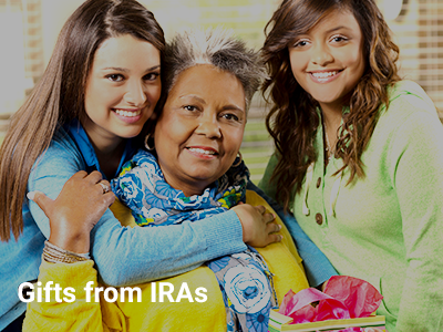 Photo of two young girls embracing an eldery woman seated in a chair, gifts from IRAs is at the bottom of the photo