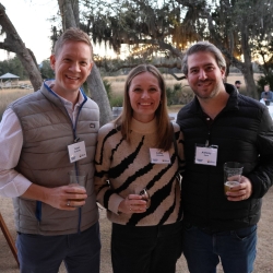 A photo of three people smiling at the camera outside at the Oyster Roast event