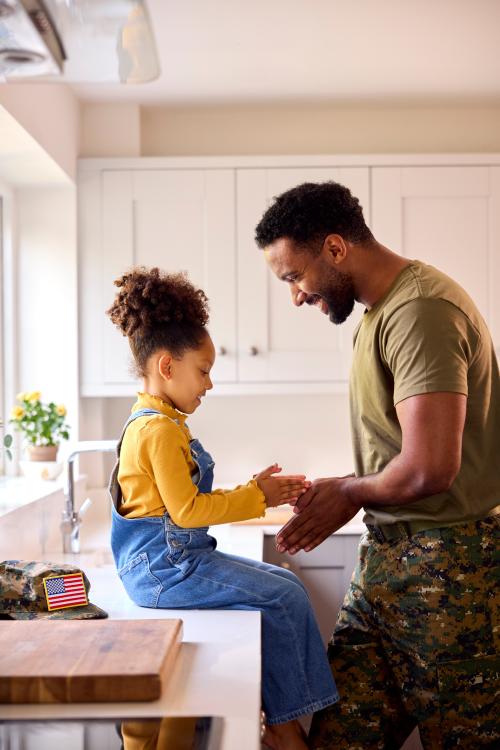 Photo of a child sitting on a countertop playing a hand game with an man wearing army fatigues