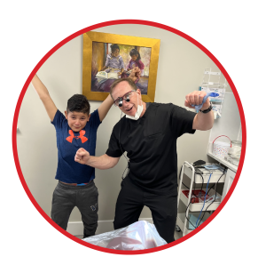 Dentist and patient cheer in front of dental equipment.