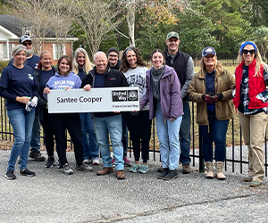 Santee Cooper employees posing for photo at project site at Days of Caring, group holding sign that says Santee Cooper with Trident United Way logo