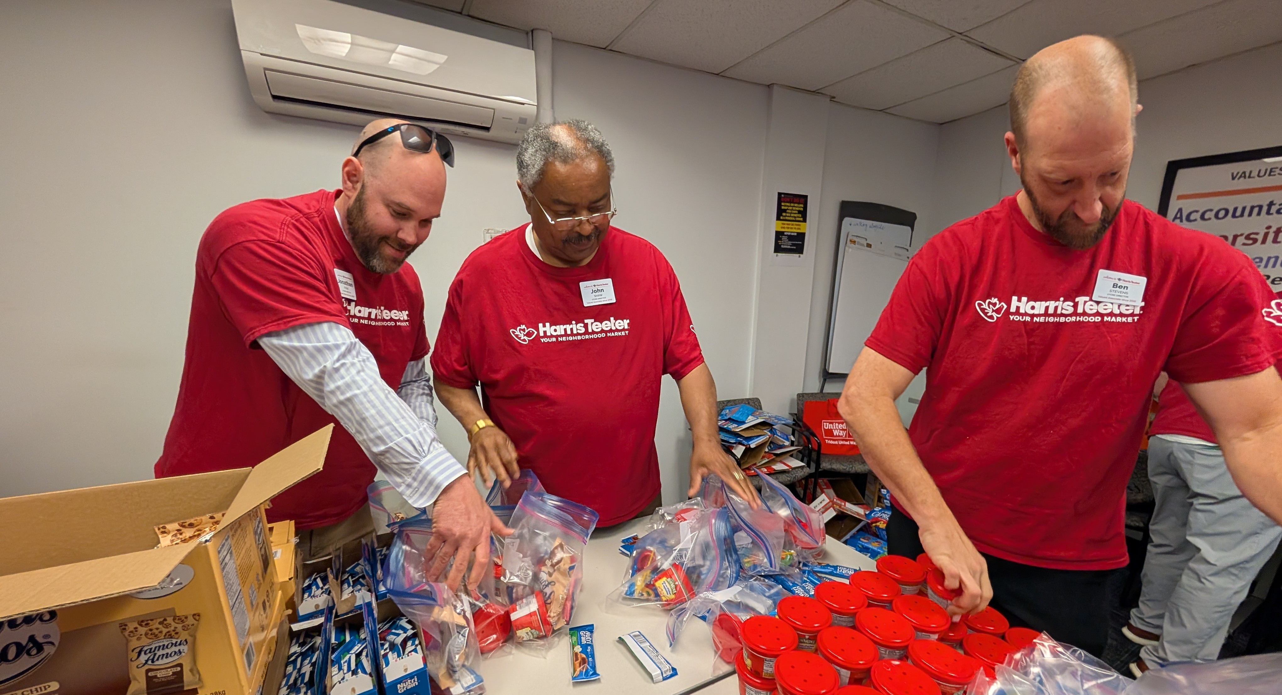 3 people in matching red tshirts pack snack bags together.