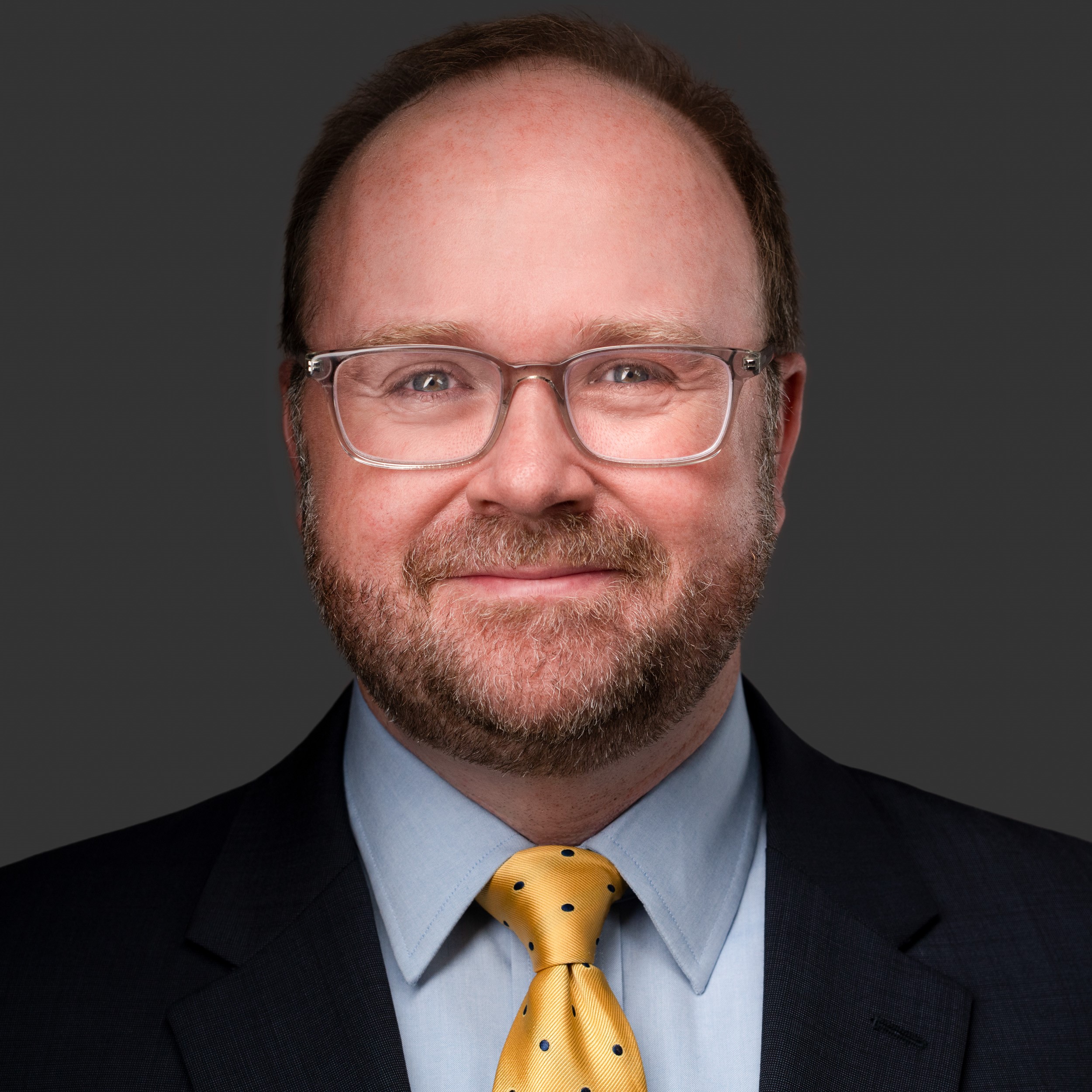 Photo of David D.J. Hampton II, wearing glasses, yellow tie, blue collared shirt, black jacket