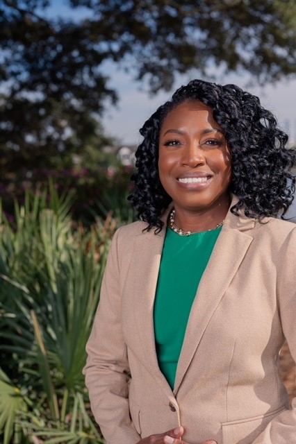 Photo of Natasha Chatman. She is outside, smiling, wearing a green shirt and beige jacket.