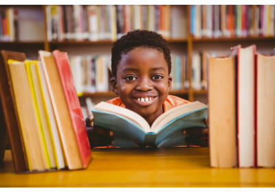 student holding open book peering through row of books at library