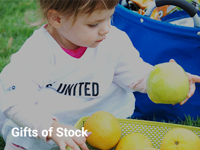 photo of a young girl outside wearing a live united shirt holding an apple from a basket, gifts of stock is written on the bottom of the photo