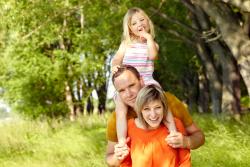 Photo of a child and parents playing outdoors in warm weather. They are posing for the camera.