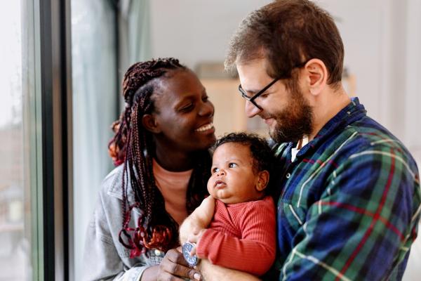 A couple holding a baby all smiling at each other in their home