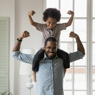 A young Black child sits on the shoulders of an adult Black man. They both are holding up their arms to flex biceps that indicates "strong". They are both smiling.