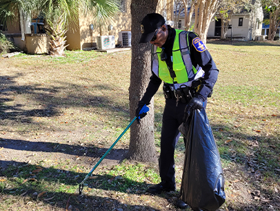 Volunteer wearing a City of Charleston police uniform using a grabber on a long pole to pick up litter on the ground outside