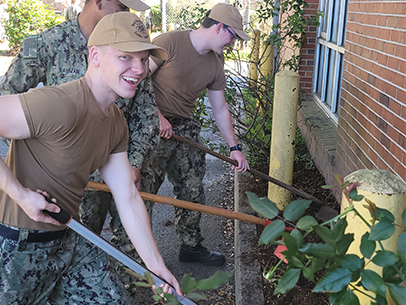 Three volunteers wearing military fatigues are digging dirt,one volunteer looks at the camera smiling.