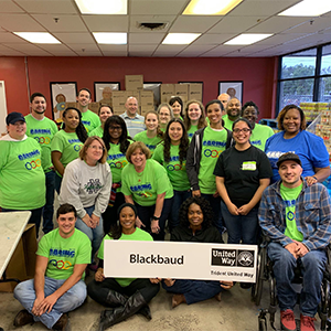 A large group of volunteers wearing bright green Day of Caring t-shirts pose for a photo at Lowcountry Food Bank. Two individuals are holding a sign that says Blackbaud.