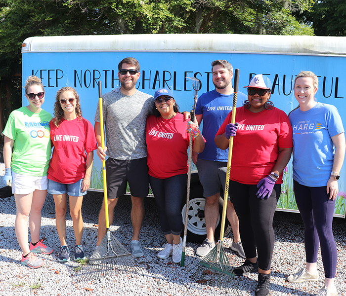 A group of seven volunteers standing in front of a truck that reads Keep North Charleston Beautiful. Volunteers are wearing Day of Caring, Live United and Elliott Davis shirts. Three of the volunteers are holding rakes in their hands. All are smiling